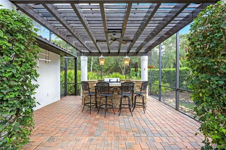 Screened-in summer kitchen featuring a built-in grill, a convenient refrigerator, and a practical sink, all elegantly situated beneath a beautifully crafted wood pergola,