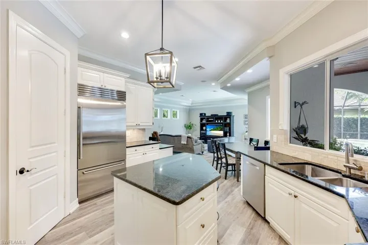 Well-appointed kitchen featuring a Sub-Zero refrigerator, an array of stainless steel appliances, granite countertops, crown molding and stylish hanging light fixtures.
