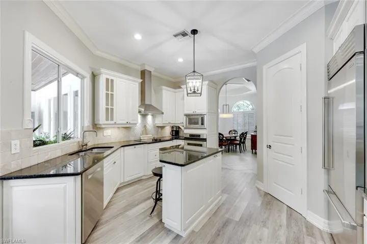Kitchen with dark stone countertops, built in appliances, white cabinetry, tasteful backsplash, and ornamental molding