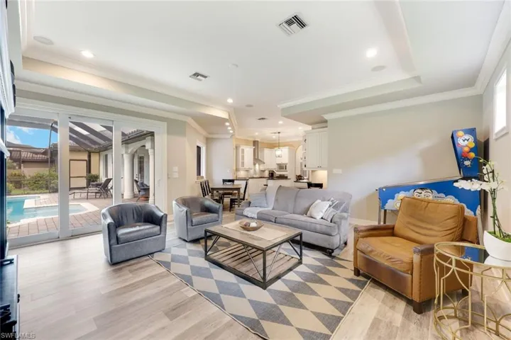 Living room featuring a raised ceiling, light wood-type flooring, ornamental molding, and recessed lighting