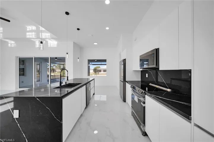Kitchen featuring marble finish floor, modern cabinets, white cabinets, a sink, and appliances with stainless steel finishes