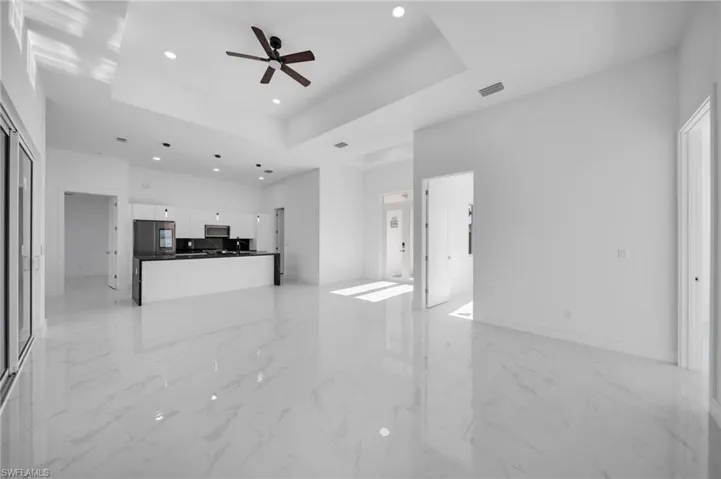 Unfurnished living room with ceiling fan, visible vents, a raised ceiling, marble finish floor, and recessed lighting