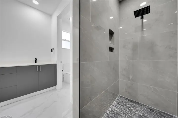 Full bath with toilet, tiled shower, marble finish floor, and vanity