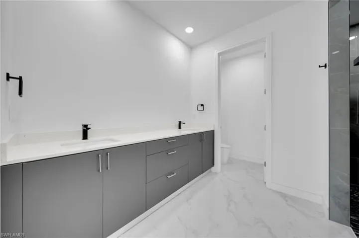 Full bath featuring double vanity, toilet, a sink, and marble finish floor