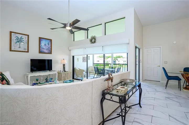 Living area featuring light marble finish flooring, a ceiling fan, and a high ceiling