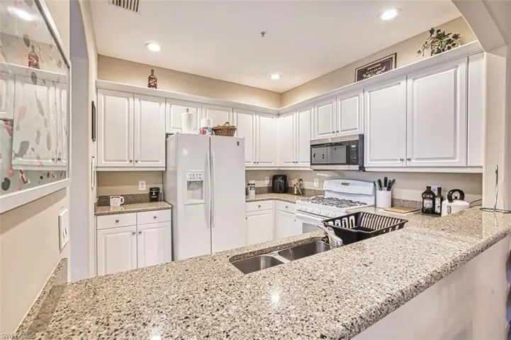 Kitchen featuring white cabinetry, granite countertops, a double basin stainless steel sink, and recessed lighting