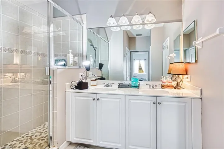 Bathroom featuring a dual vanity with white cabinetry, a large mirror, and a glass-enclosed shower with tiled walls and a decorative accent strip