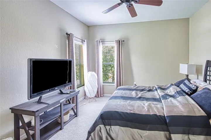Carpeted room featuring a ceiling fan, two windows with blinds and drapes, and neutral wall tones