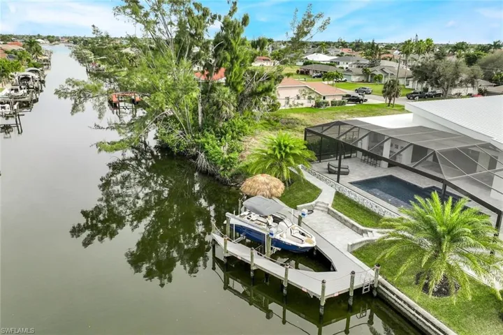 Dock area with boat lift, a water view, a lanai, a pool, and a residential view