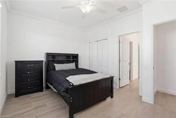Bedroom with wood finish floors, crown molding, a ceiling fan, and a closet