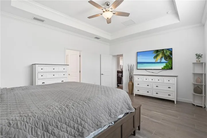Bedroom with ornamental molding, a tray ceiling, wood finished floors, and a ceiling fan