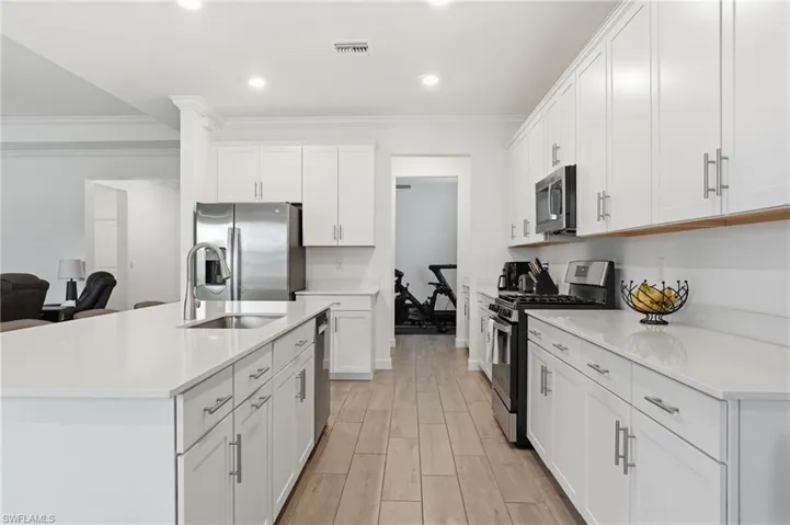 Kitchen featuring stainless steel appliances, a kitchen island with sink, wood finish floors, crown molding, and white cabinets