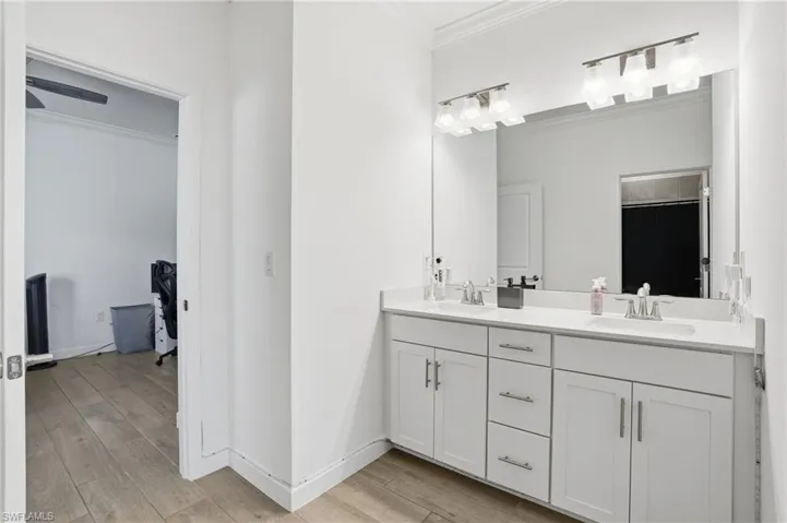 Full bath featuring ornamental molding, double vanity, and light wood finished floors