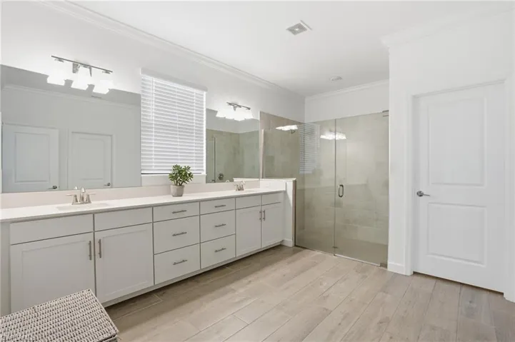 Full bath with a shower stall, double vanity, light wood-type flooring, and ornamental molding