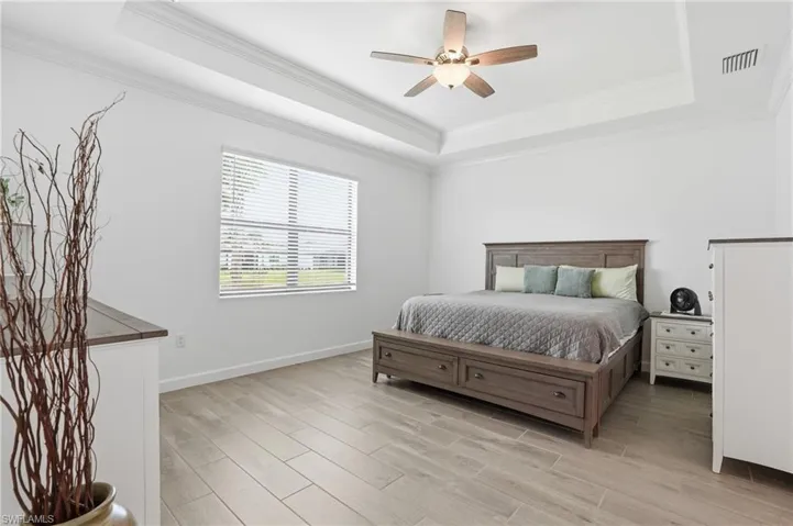 Bedroom featuring crown molding, wood finish floors, ceiling fan, and a raised ceiling