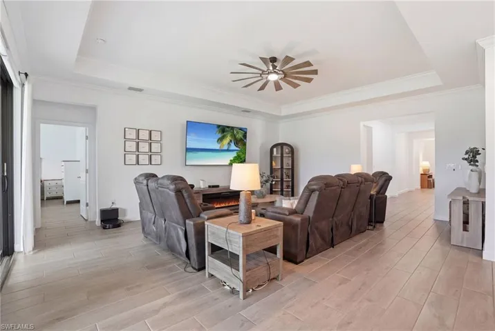 Living room with wood finish floors, a raised ceiling, crown molding, and ceiling fan