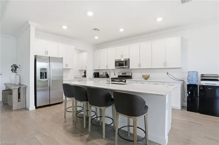 Kitchen featuring stainless steel appliances, light wood-style floors, white cabinets, crown molding, and a kitchen bar