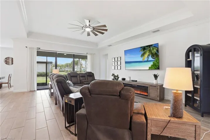 Living area with a raised ceiling, wood finish floors, ceiling fan, ornamental molding, and a glass covered fireplace
