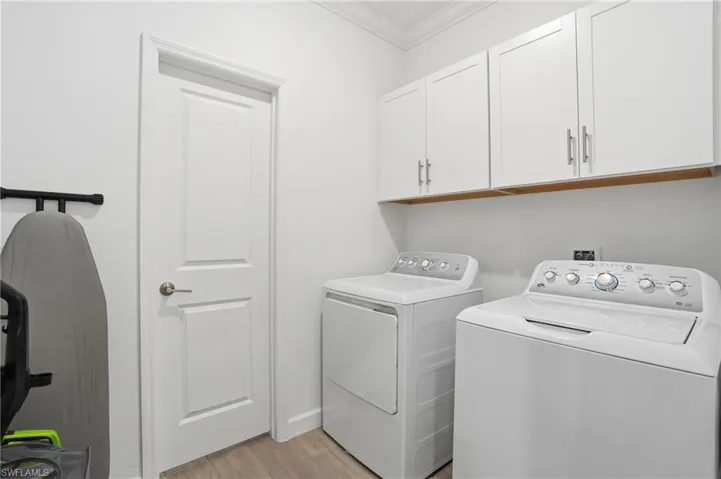 Laundry area featuring crown molding, light wood finished floors, washer and dryer, and cabinet space