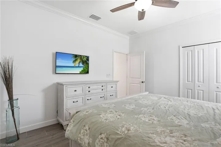 Bedroom with crown molding, dark wood-style floors, a ceiling fan, and a closet