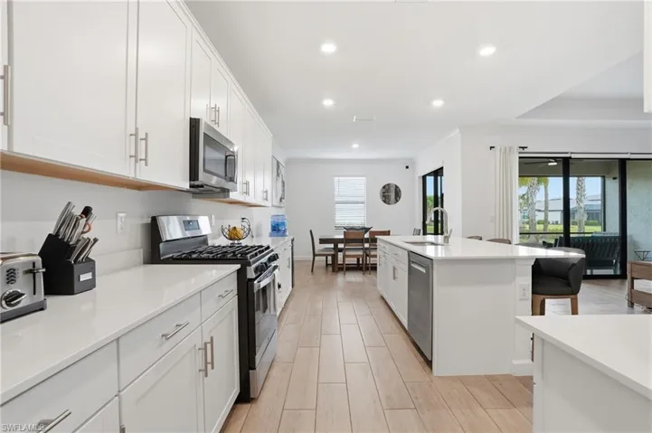 Kitchen with stainless steel appliances, white cabinetry, wood finish floors, a center island with sink, and recessed lighting