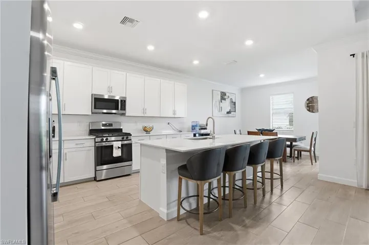 Kitchen with stainless steel appliances, white cabinets, wood finish floors, a kitchen island with sink, and crown molding