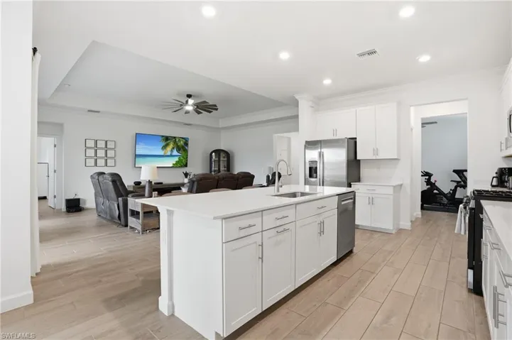 Kitchen with wood tiled floors, ornamental molding, an island with sink, open floor plan, and stainless steel appliances