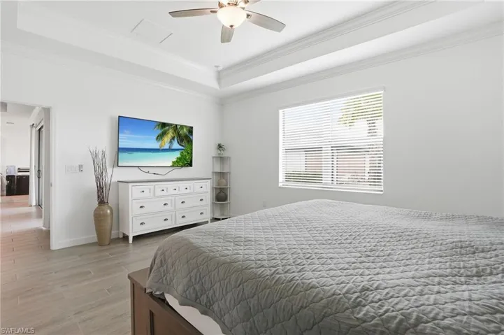 Bedroom featuring light wood-style floors, crown molding, a ceiling fan, and a tray ceiling