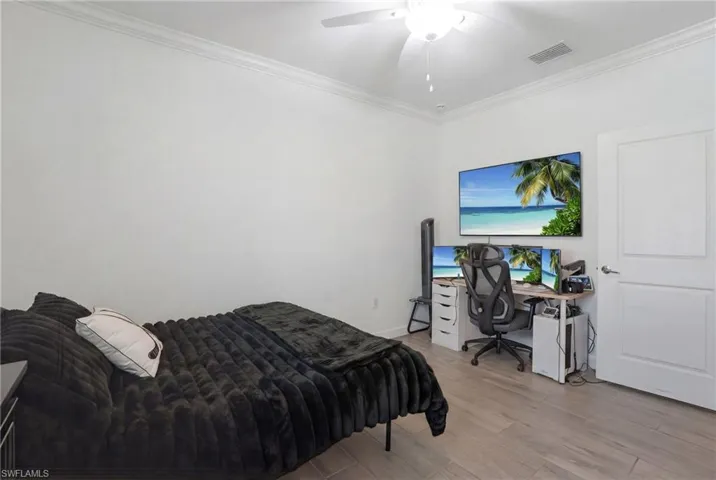 Bedroom with light wood finished floors, a desk, ornamental molding, and a ceiling fan