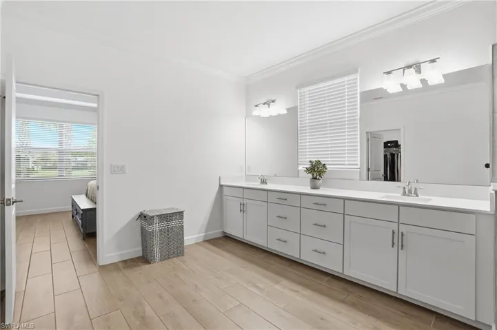 Full bath with double vanity, connected bathroom, light wood-style floors, crown molding, and a walk in closet