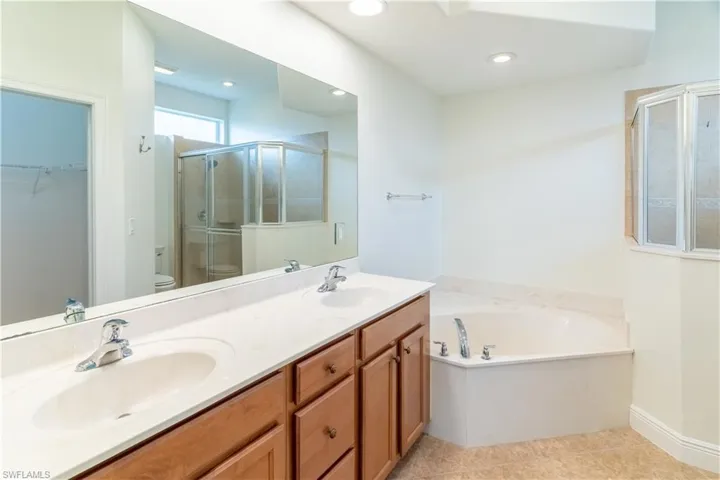 Full bathroom with a spacious closet, a bath, double vanity, a shower stall, and light tile patterned flooring