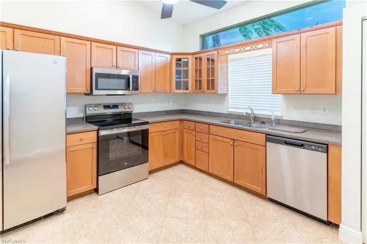 Kitchen with stainless steel appliances, glass insert cabinets, a ceiling fan, and light tile patterned floors