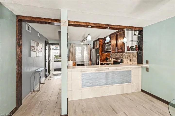 Kitchen with wood finish floors, stainless steel appliances, light countertops, beam ceiling, and decorative backsplash