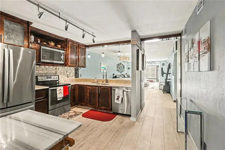 Kitchen featuring stainless steel appliances, dark wood finish cabinetry, wood tiled floors, decorative backsplash, and track lighting