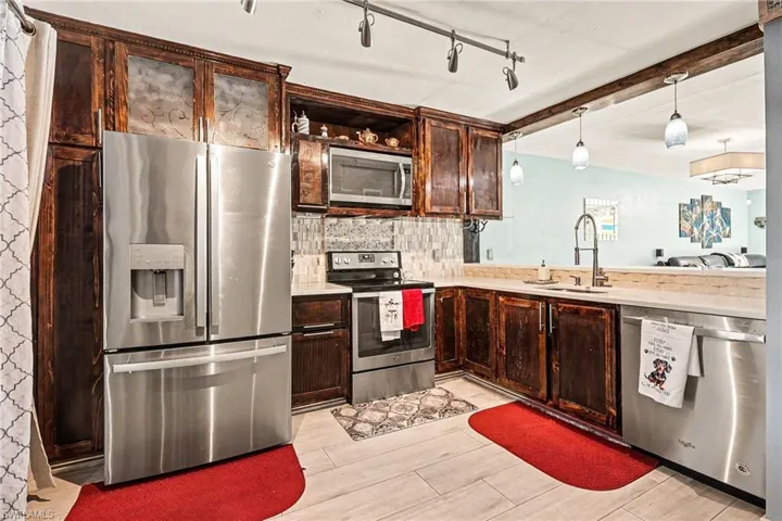 Kitchen with stainless steel appliances, dark wood finish cabinets, wood finish floors, backsplash, and open shelves