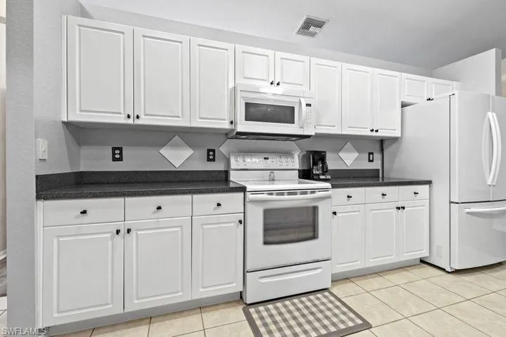 Kitchen with white cabinets, light tile patterned flooring, and white appliances