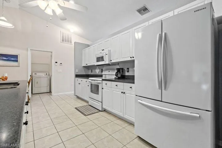 Kitchen featuring lofted ceiling, white cabinets, white appliances, and light tile patterned flooring