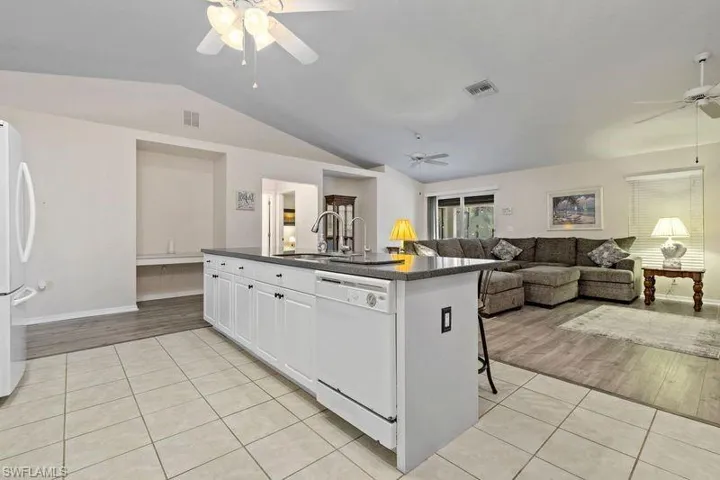 Kitchen with ceiling fan, light hardwood / wood-style flooring, white cabinets, vaulted ceiling. Never feel along when you can interact in this large great room space