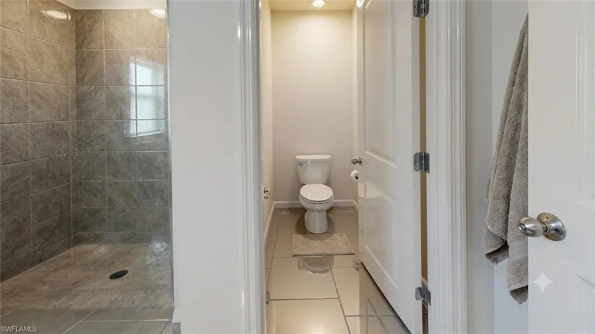Bathroom featuring a fully tiled shower with a window, a separate toilet area with recessed lighting, and large format floor tiles