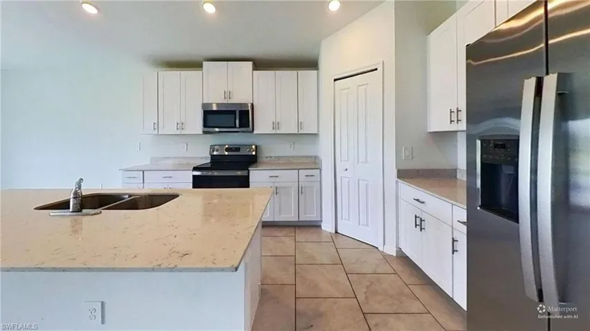 Kitchen featuring a central island with an undermount dual-basin sink, light-toned countertops, white cabinetry with dark hardware, stainless steel appliances, and tiled flooring