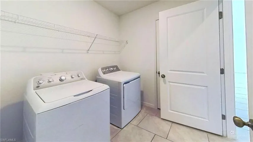 Laundry area featuring light-toned walls, tile flooring, and overhead wire shelving
