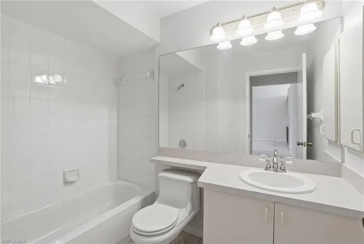 Full bathroom featuring a white bathtub with tiled surround, a toilet, and a vanity with an integrated sink and countertop