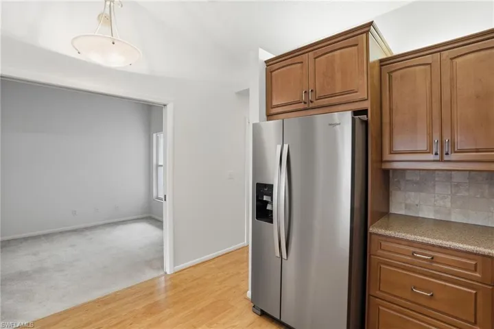 Kitchen area featuring wood-finish flooring, stainless steel refrigerator, wood cabinetry, stone-look countertop, and tile backsplash