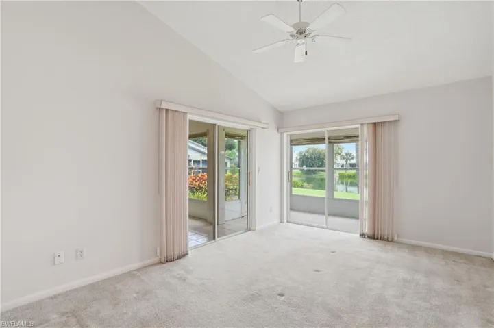 Vaulted ceiling room featuring light-colored carpet, a ceiling fan, and two sets of sliding glass doors
