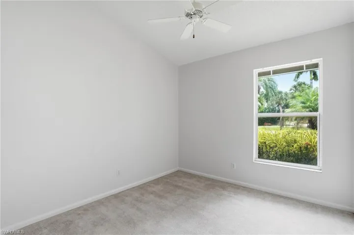 Carpeted room featuring a vaulted ceiling with a ceiling fan, a window with exterior landscaping, and light gray wall paint