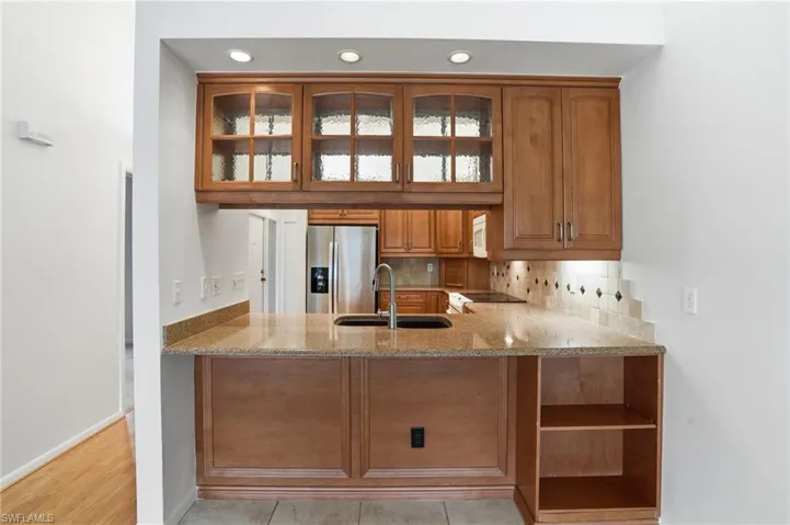 Kitchen pass-through featuring warm wood-finish cabinetry, illuminated glass-front upper cabinets, and recessed lighting