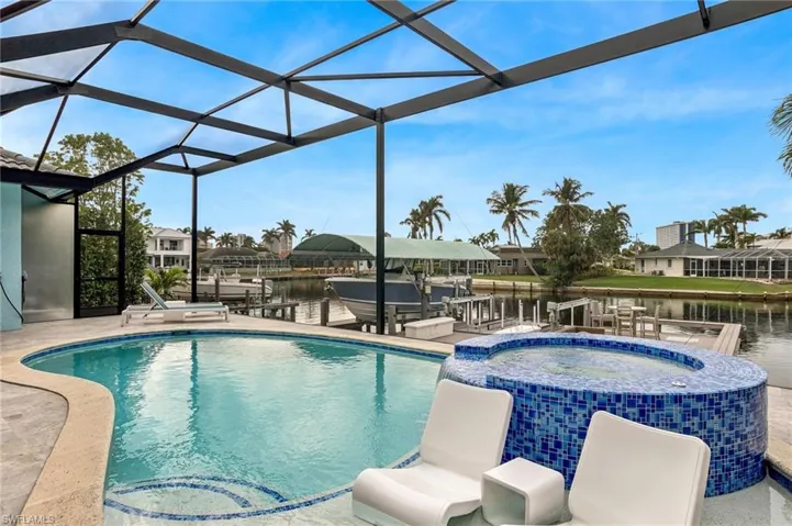 View of swimming pool featuring an in ground hot tub, a patio, a water view, and glass enclosure