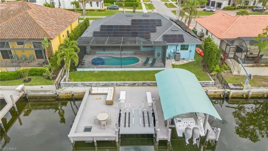 Back of property featuring a swimming pool with hot tub, a water view, glass enclosure, a patio area, and a yard