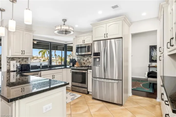 Kitchen with tasteful backsplash, light tile patterned floors, stainless steel appliances, and decorative light fixtures