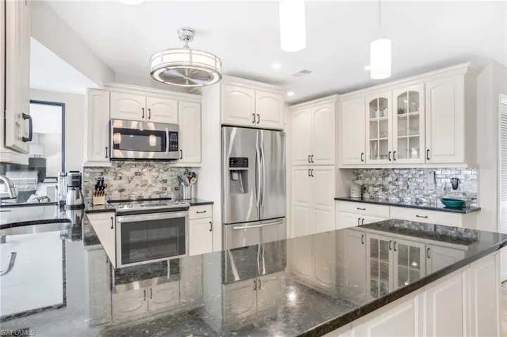 Kitchen with dark stone counters, white cabinets, hanging light fixtures, decorative backsplash, and stainless steel appliances